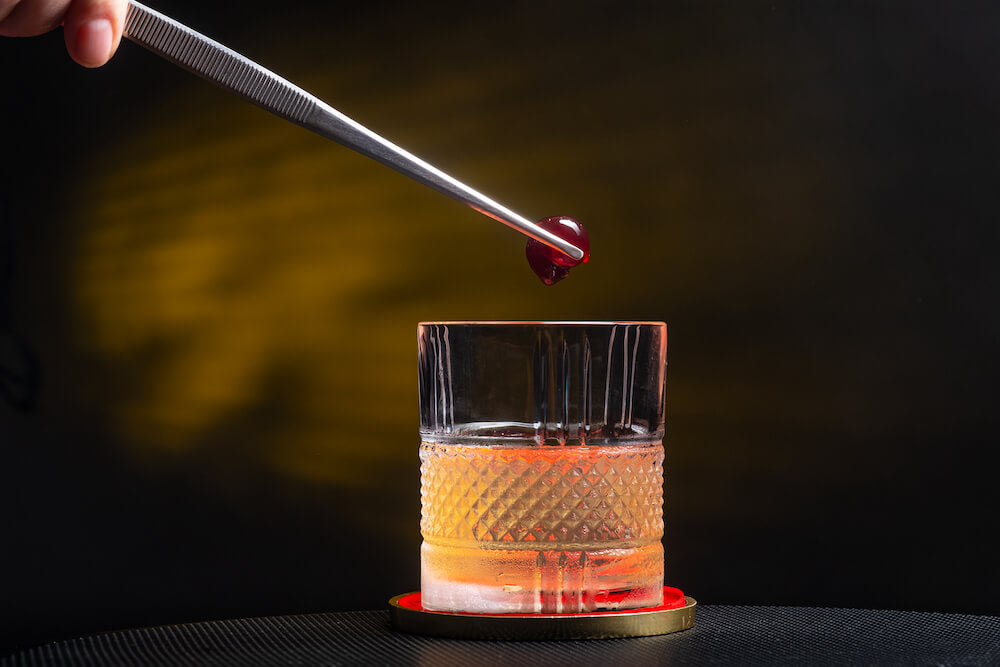 Mixologist dropping a cherry into a cocktail.