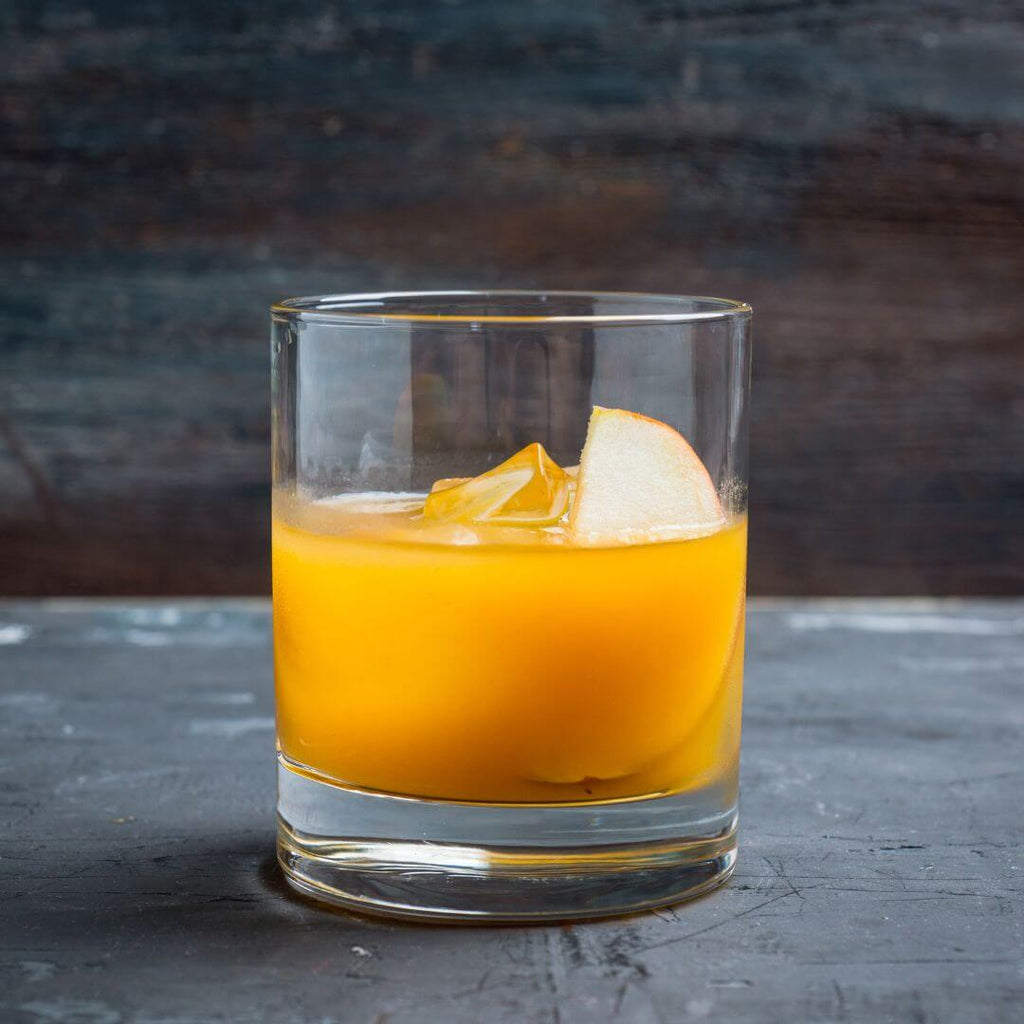 Up close of a yellow cocktail with an apple garnish.