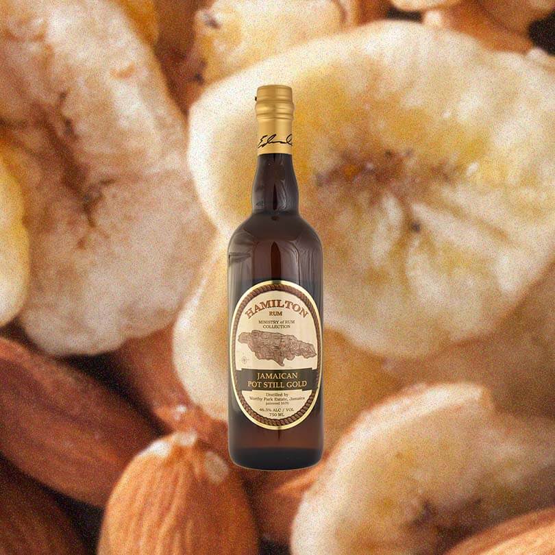 Bottle of Hamilton Jamaican Pot Still Gold Rum over backdrop image of bananas and almonds.