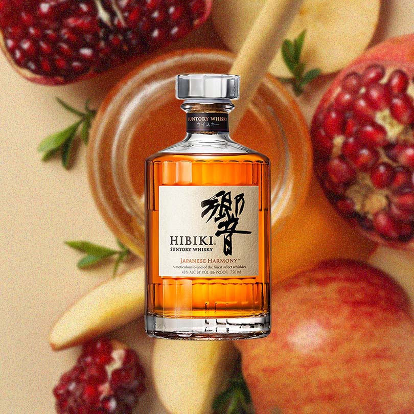 Bottle of Hibiki Japanese Harmony Whisky over back drop mage of fruits and honey on a table.