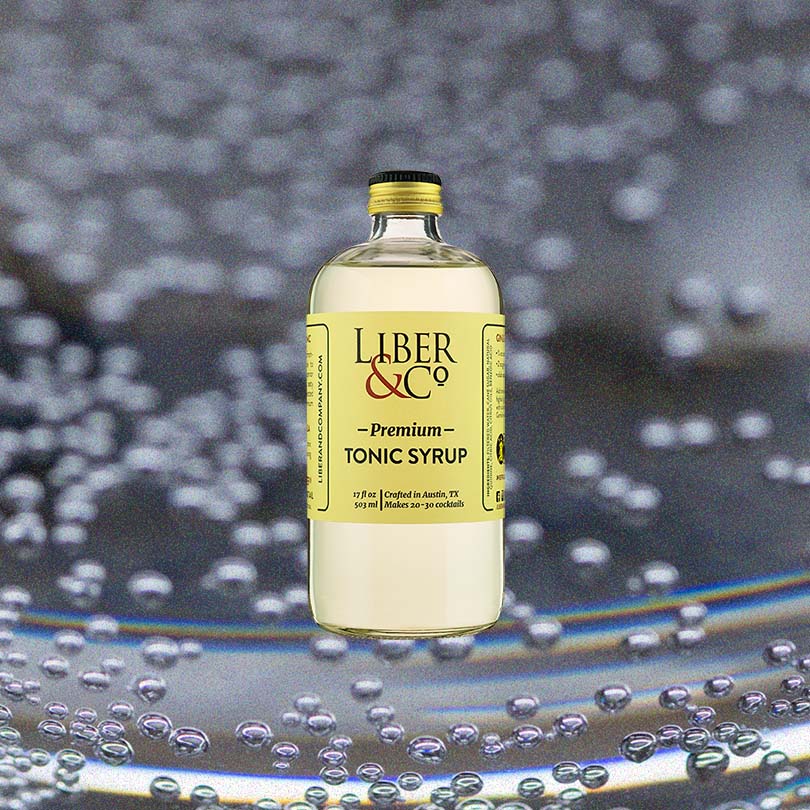 Bottle of Liber & Co. Premium Tonic Syrup over backdrop of water droplets.