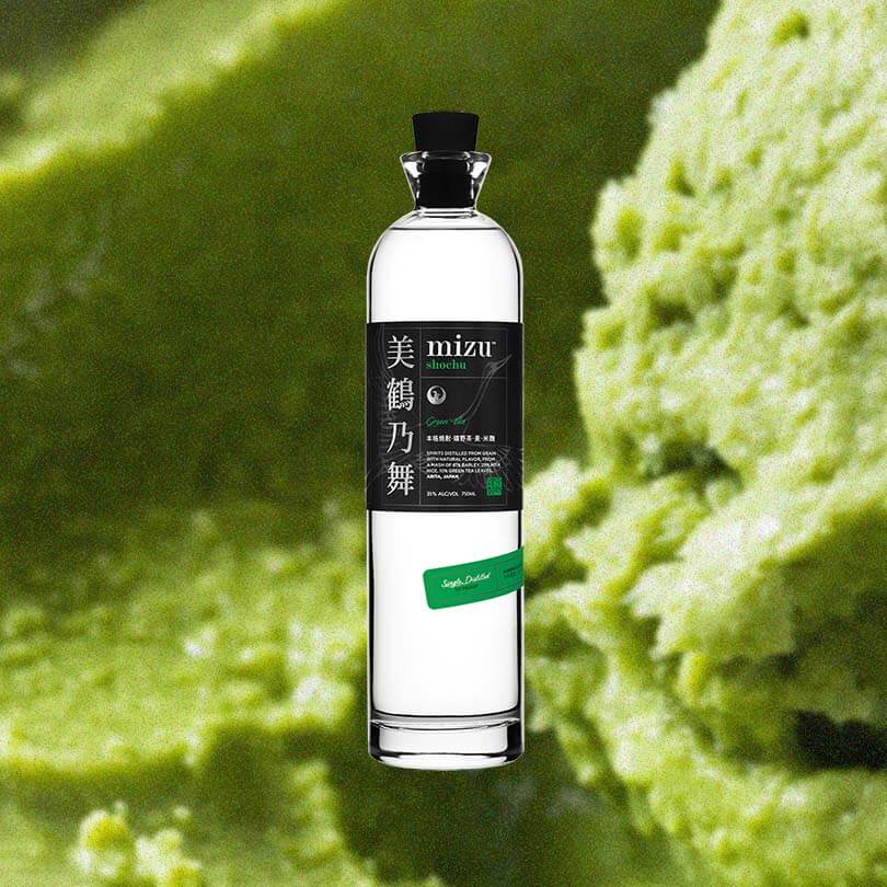 A lovely tall thin bottle with a black cap. The label is black with Japanese characters on the left side. It reads in English: Mizu Shochu Green Tea. This is against a macro shot of delicious looking matcha sorbet.