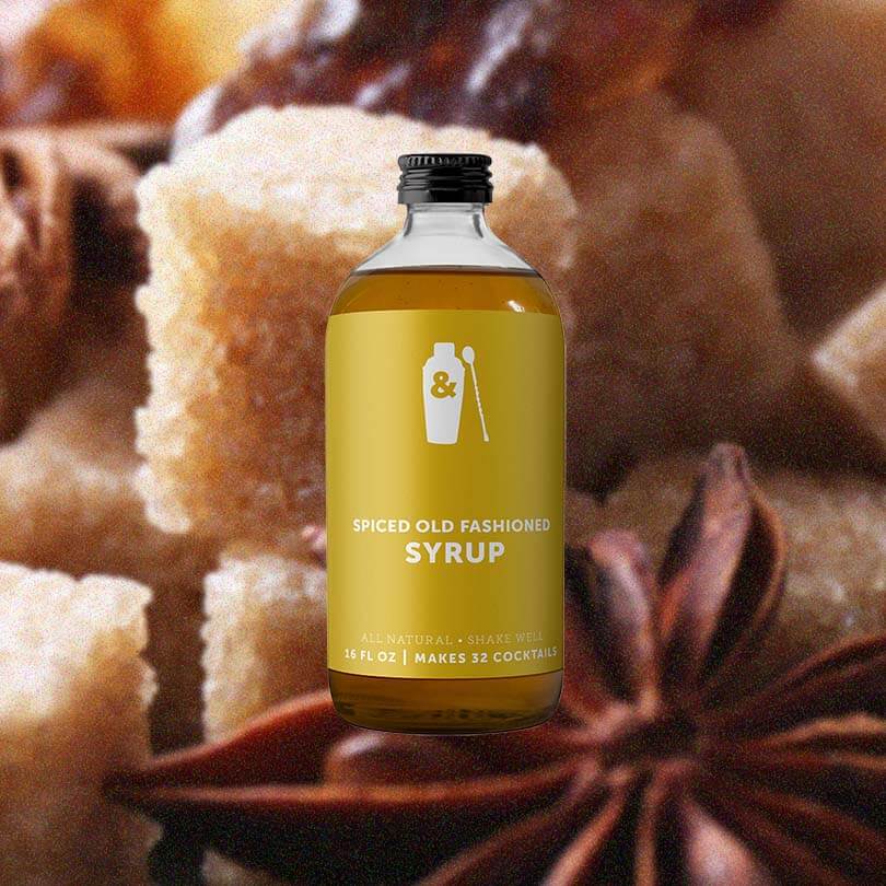 Bottle of Shaker & Spoon Spiced Old Fashioned Syrup over backdrop of spices.