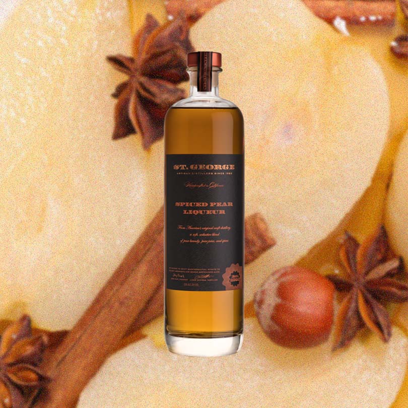 Bottle of St. George Spiced Pear Liqueur over backdrop of spices.