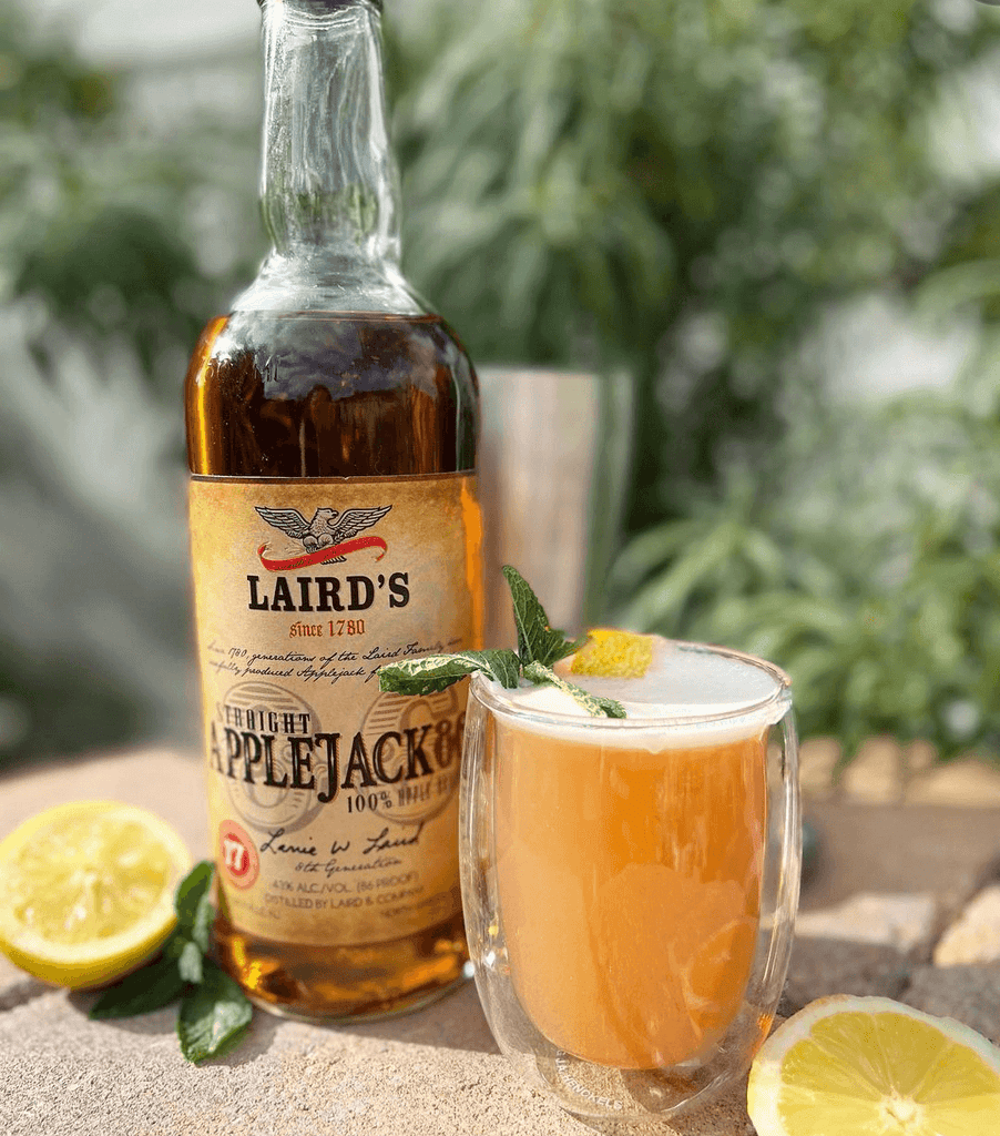 Bottle of Laird's Straight Applejack 86 on an outdoor table next to a cocktail.