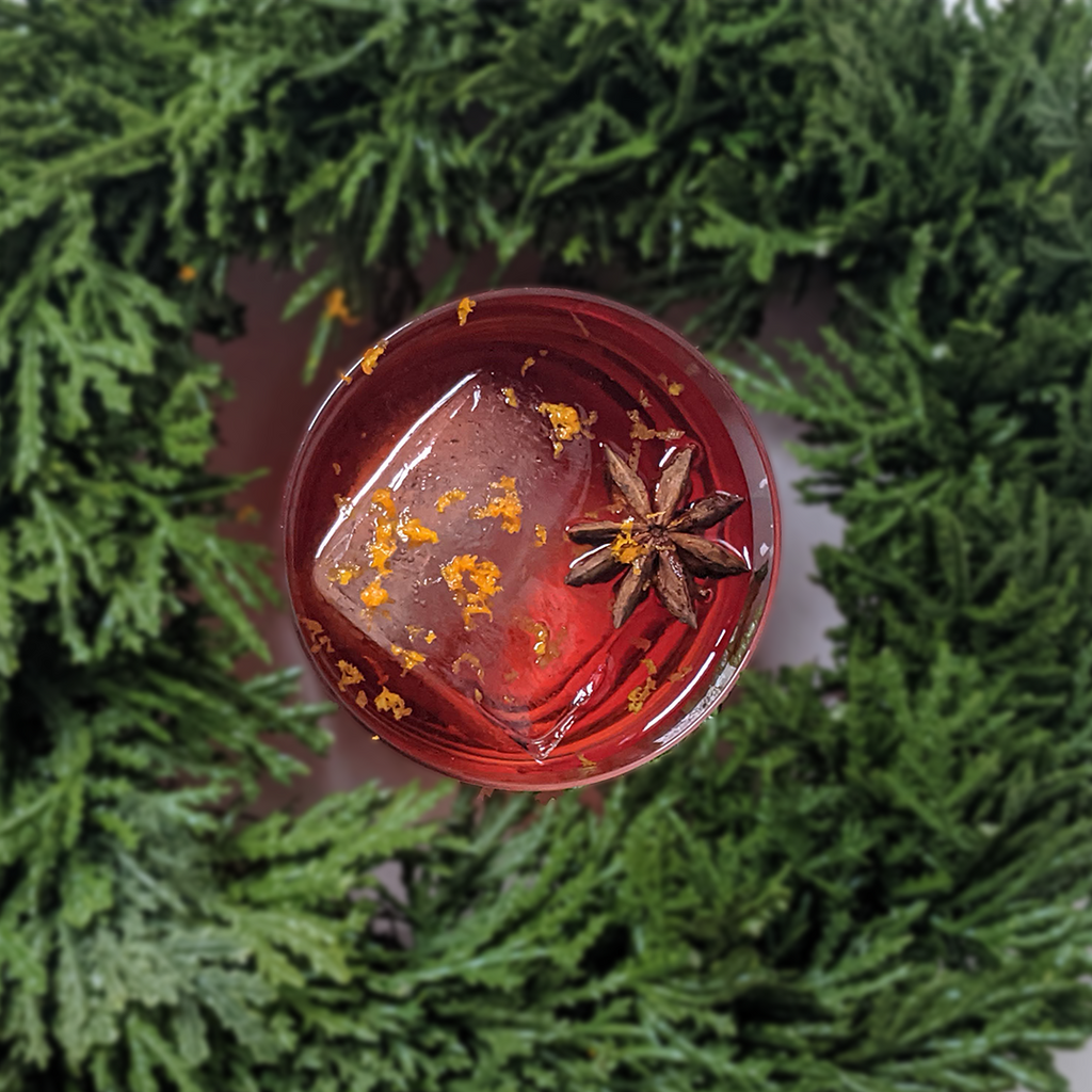 Holiday Negroni cocktail, surrounded by evergreen wreath.