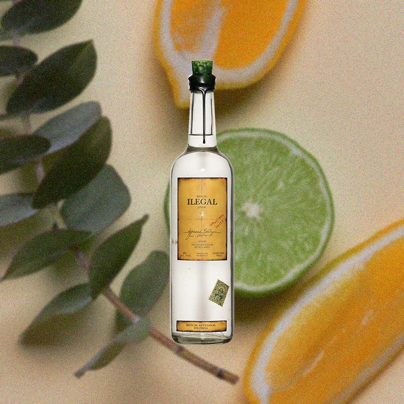 Bottle of Ilegal Mezcal Joven over backdrop image of a lime and lemon.