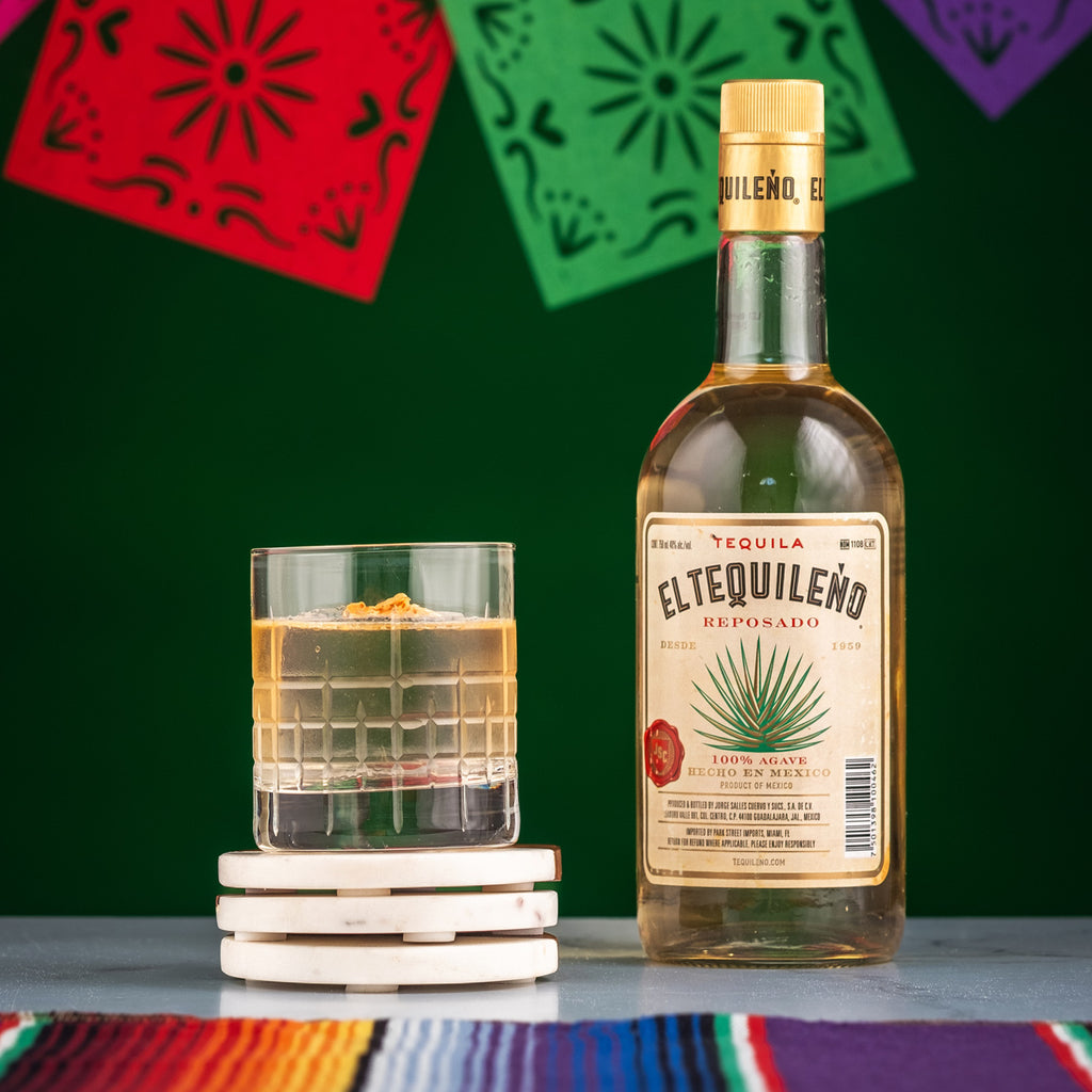 Bottle of El Tequileno Reposado on a table next to a cocktail.