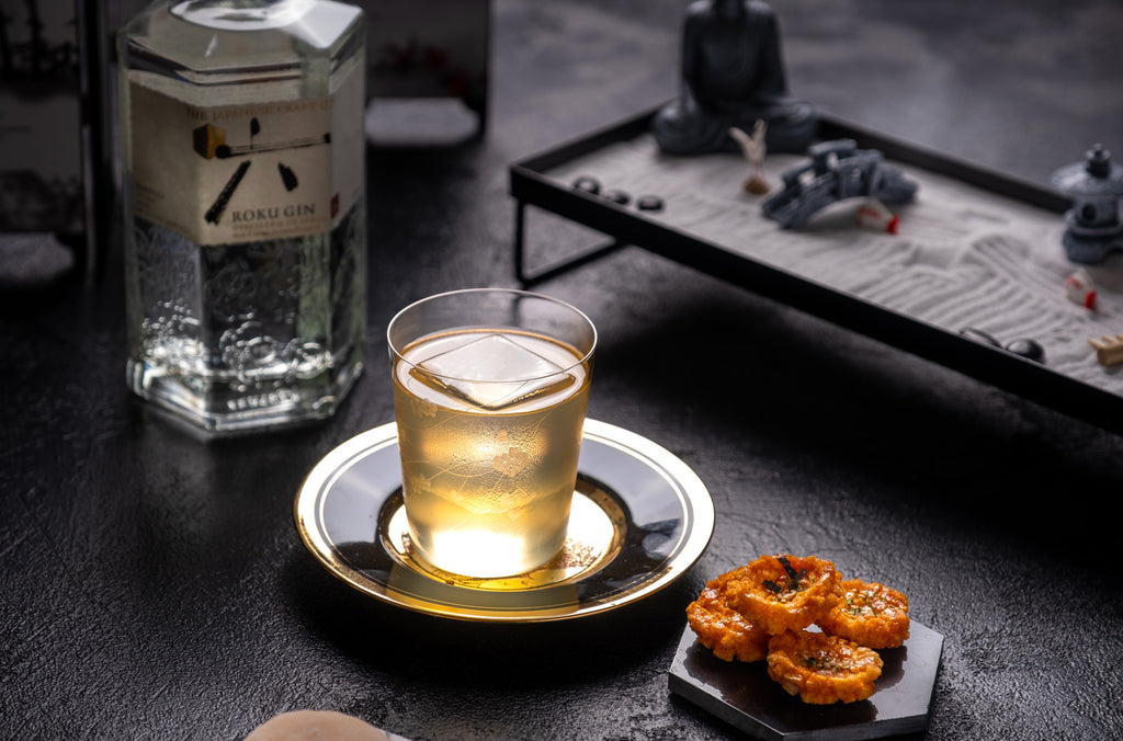 Cocktail in small glass on gold plate sitting on stone countertop.