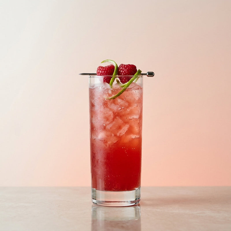 A photo of the Raspberry Baja Cooler cocktail containing Milagro Reposado Tequila, Chambord Liqueur, Cranberry juice, AquaRiva Organic Agave Syrup, Freshly squeezed lime juice, Raspberries in a Collins.