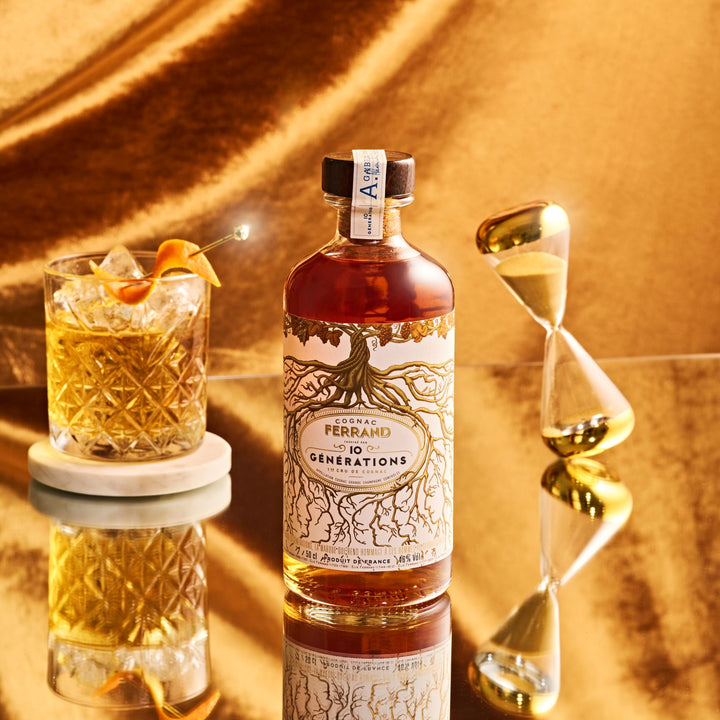 Bottle of Ferrand 10 Generations rum with a cocktail and hourglass on a reflective surface.
