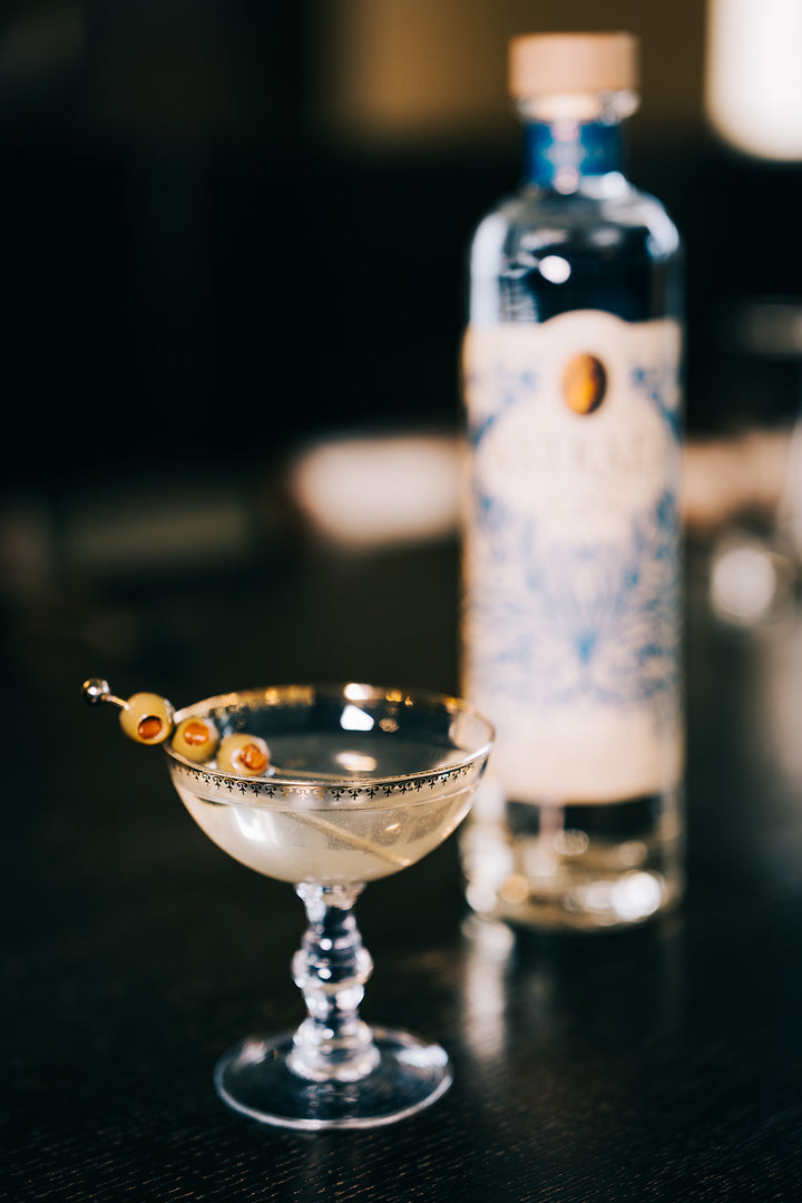 Cocktail in a glass with garnishes next to a bottle on a dark surface