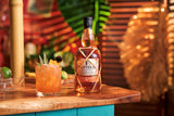 Bottle of Planteray 5 Year Rum on a wooden bar with a cocktail garnished with fruit
