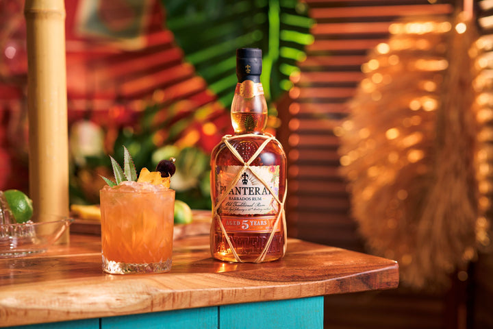 Bottle of Planteray 5 Year Rum on a wooden bar with a cocktail garnished with fruit