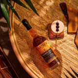 Bottle of Planteray Original Dark Rum  on a woven surface with a cocktail garnish.
