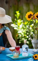 Woman drinking a cocktail made with 1615 Pisco outside by a table with bright sunflowers.