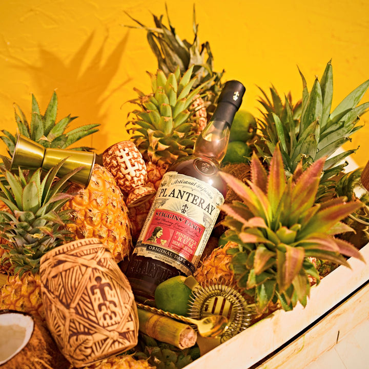 Bottle of Planteray Stiggin's Fancy Rum surrounded by pineapples and decorative items on a yellow background