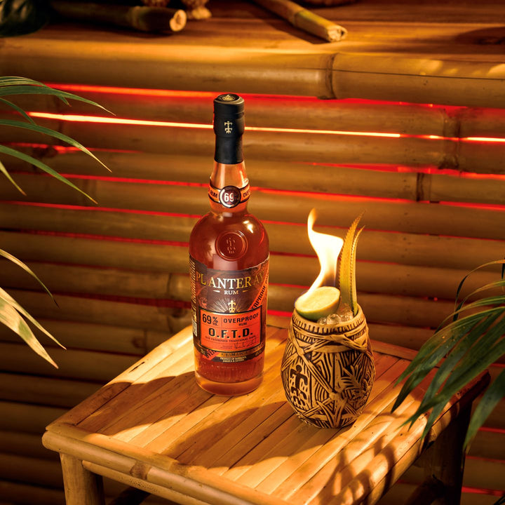 Bottle of Planteray rum on a wooden table with a lit candle in the background