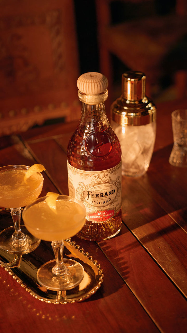 Bottle of Ferrand Cognac on a bar with cocktails and a shaker.