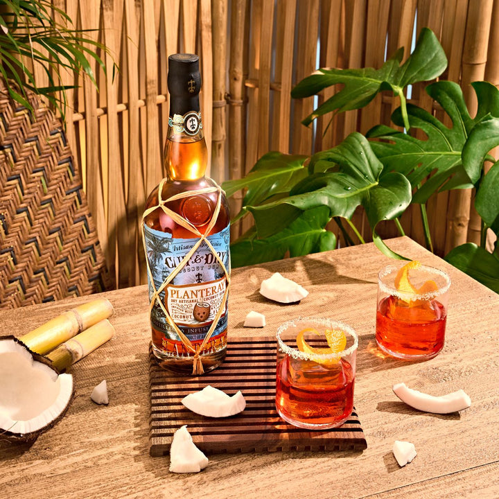 Bottle of Planteray Diplomatico rum with two cocktails on a wooden table outdoors.