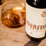 Bottle of Ardamar amaro with a glass containing the drink on a wooden surface