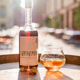Bottle and glass of Cardamar wine on a wooden surface with a blurred outdoor background