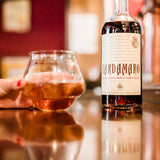 Bottle of Cardamaro with a glass of the product on a reflective surface.
