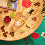 Bottle of Planteray 3 Stars rum on a woven surface with limes, raspberries, and dominoes.