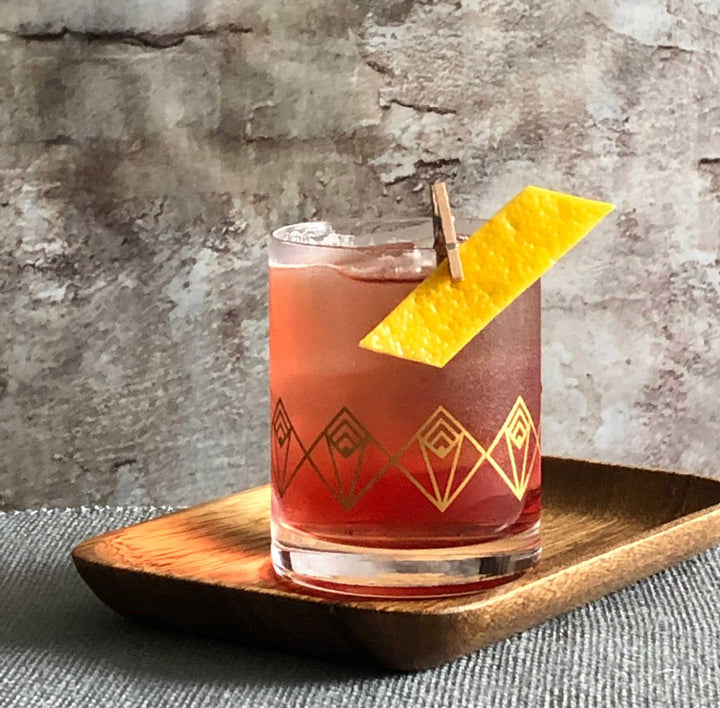 Red cocktail with geometric design in a glass on a wooden coaster against a textured gray background