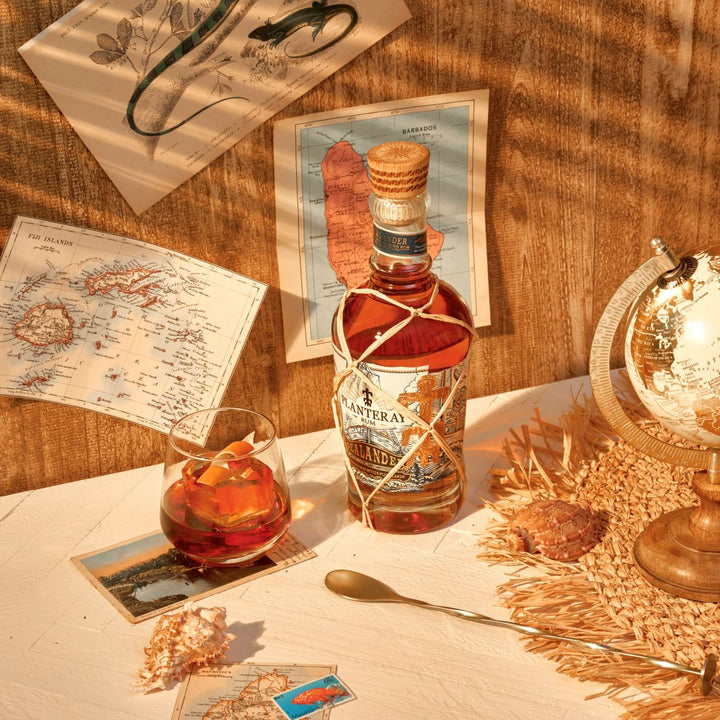 Bottle of Planteray rum on a table with a cocktail and decorative items