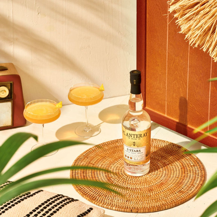 Bottle of Planetary Spirits 3 Stars on a woven coaster with two cocktails in the background.