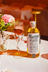Bottle of Rockey's Botanical Liqueur on a table next to a rose shaped cocktail glass.