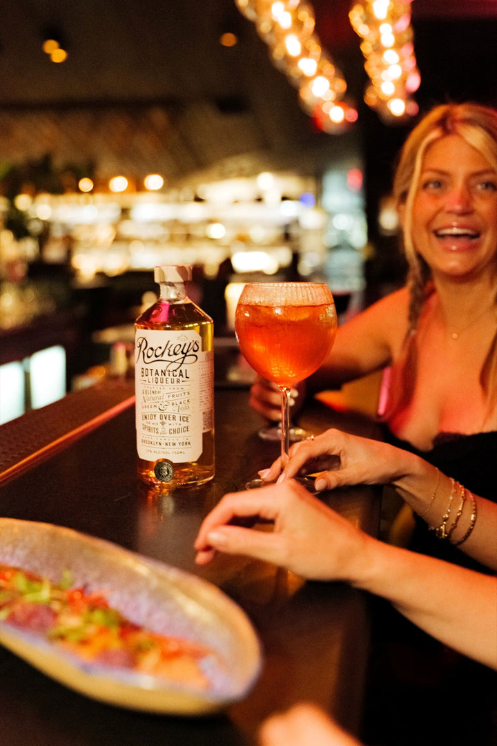 Bottle of Rockey's Botanical Liqueur on a bar 2 people are sitting at.