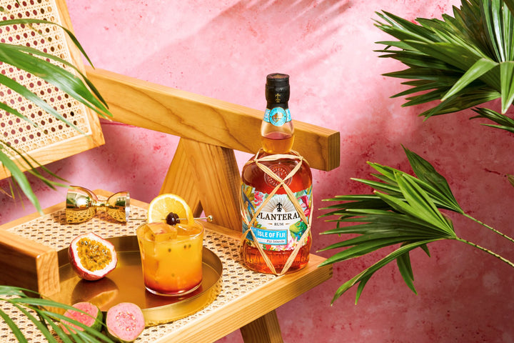 Bottle of Planteray Walk of Rum on a tray with a cocktail and tropical decorations against a pink background