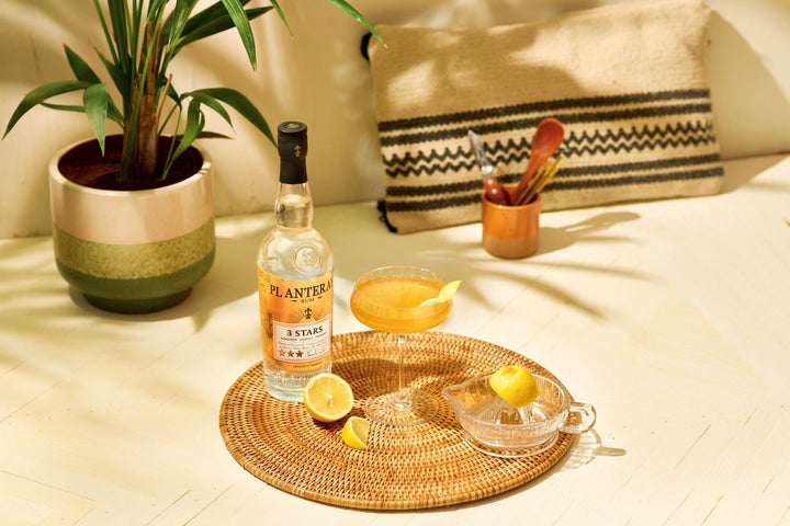 Cocktail with a bottle of Planteray 3 Star Rum on a woven coaster with a lemon wedge.