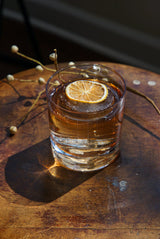 Glass of amber liquid with a lemon wheel on a wooden surface