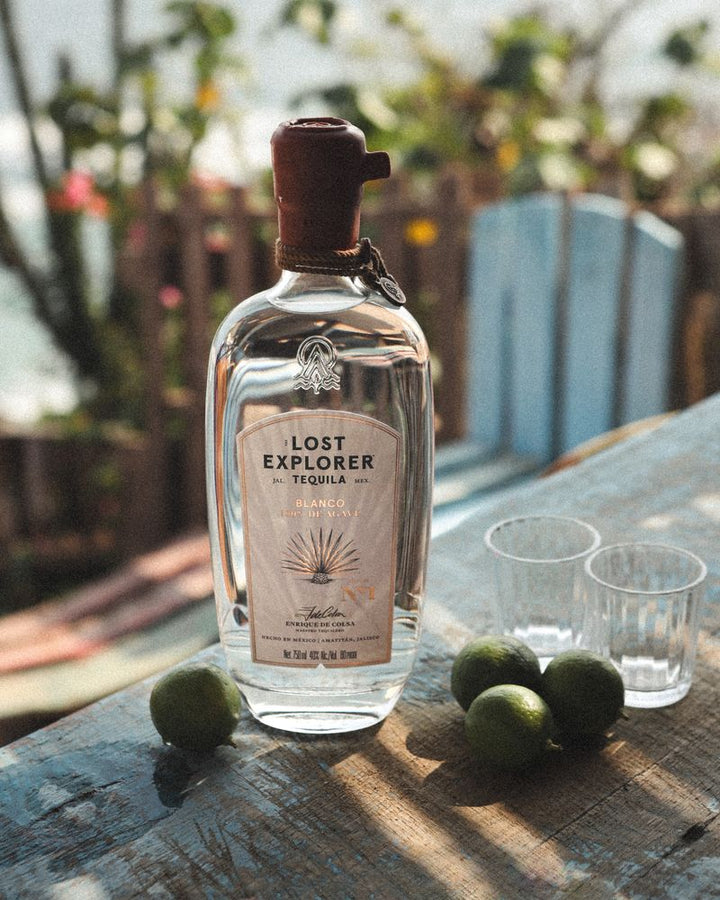 Lost Explorer tequila bottle with limes on a wooden table outdoors