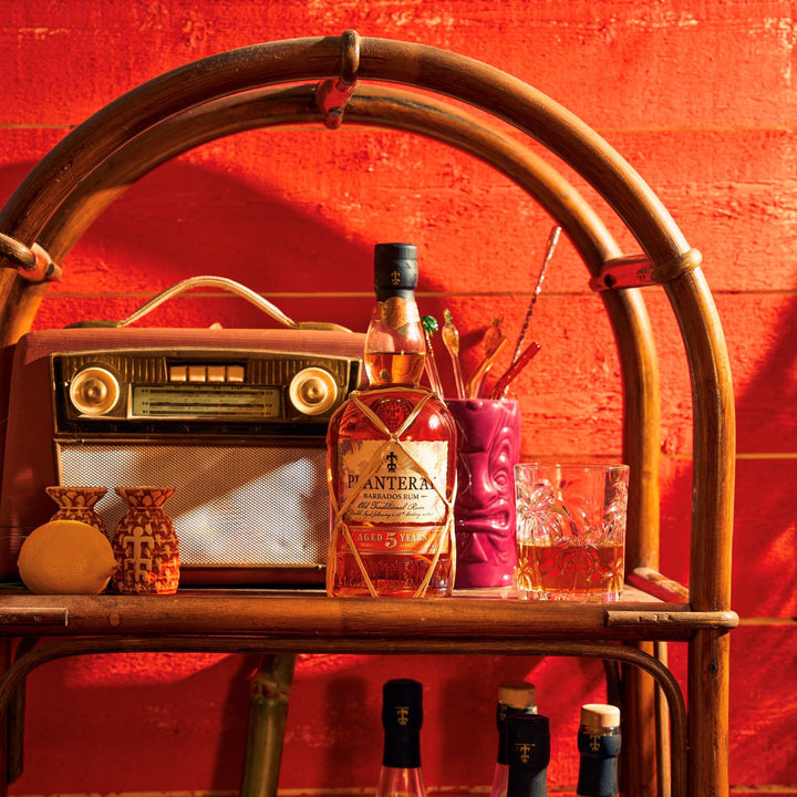 Bottle of Planteray 5 Year Rum on a bar cart with a red background