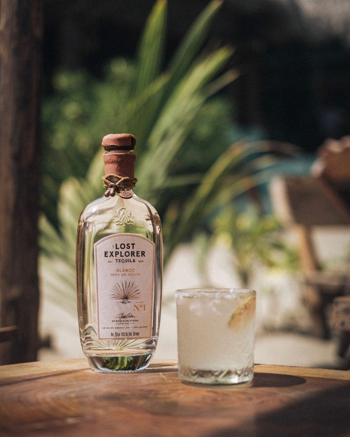 Lost Explorer tequila bottle with a glass of cocktail on a wooden surface outdoors.