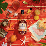 Bottle of Planteray rum on a red surface with lemons, flowers, and decorative items.