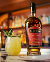 Bottle of El Dorado 5 Year Old Rum with a cocktail garnished with mint and lime on a bar.
