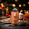 A bottle of Shaker & Spoon Gingerbread Syrup in a cozy holiday living room setting, with ginger cookies, cinnamon sticks, and various spices and flavors arranged artfully around it.