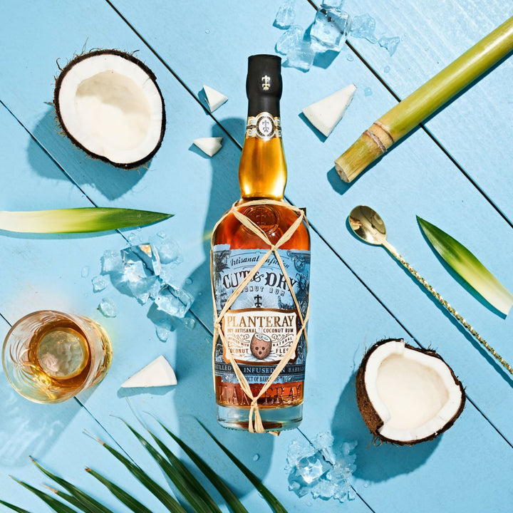 Bottle of Planteray rum with coconuts, ice, and a glass on a blue wooden surface