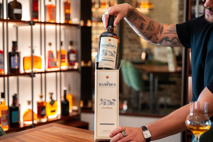 Person holding a Hampden Rum bottle in a bar setting