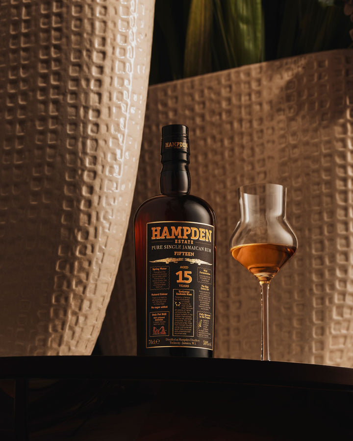 Hampden rum bottle with a glass of whiskey on a textured surface