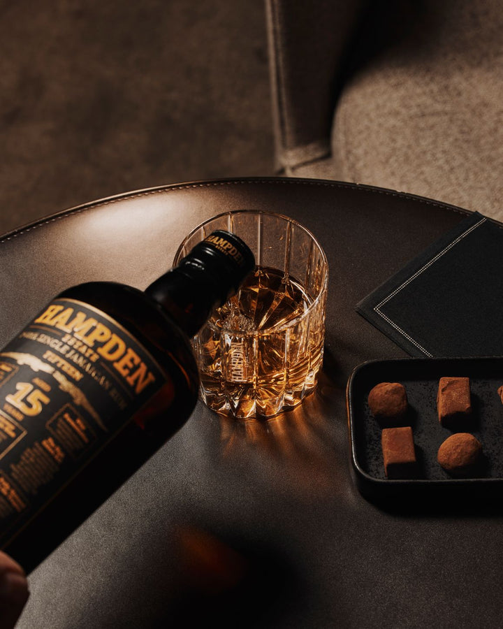 Hampden 15 Year Old whisky bottle with a glass of rum on a table with truffles.
