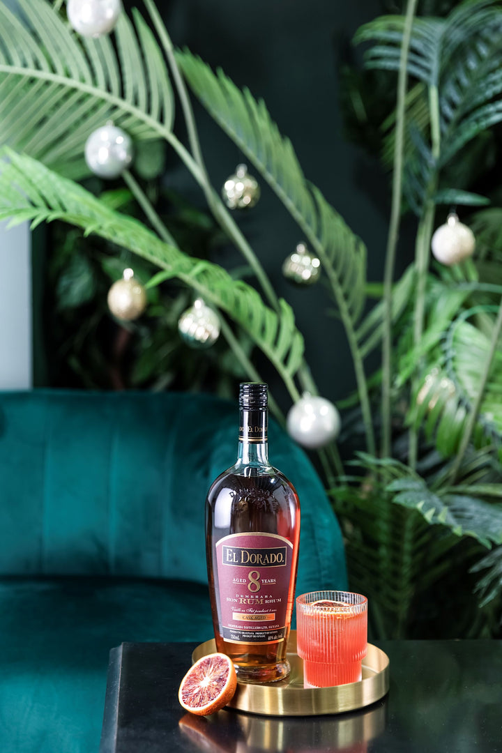 Bottle of El Dorado rum with a cocktail on a table with greenery in the background