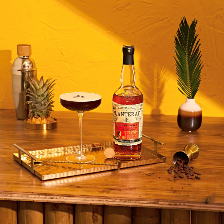 Bottle of Planteray Stiggin's Fancy Rum on a wooden table with a drink and decorative elements.
