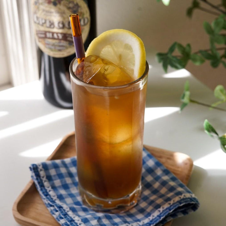 Glass of iced tea with lemon wedge on a checkered cloth, with a bottle in the background.