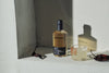 A still life with Pasille Mixe chiles, a short glass featuring a margarita with a side that's been rolled in tajin, and a bottle of Empirical Spirits Ayuuk. Loveloy light across the image, a bare concrete background.
